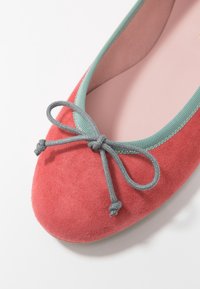 Korallfärgad mocka balett sko med en kontrasterande mintgrön kant och en grå rosettdetalj framtill, med rund tå och slät innersula.