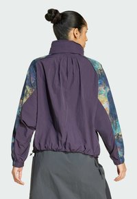 Purple windbreaker jacket featuring colorful patterned sleeves, elastic hem, high collar, and soft texture. Practical design with zippers.