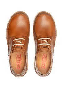 Scarpe in pelle tan con punta arrotondata, due fori per i lacci, cuciture a contrasto e una superficie liscia. Logo visibile sulle solette.