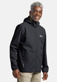 Veste softshell noire avec fermeture éclair sur le devant, capuche ajustable et deux poches latérales. Présente un logo 'Texashield' sur l'ourlet. Texture lisse.