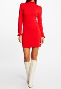 Rode jurk met lange mouwen, een hoge gerimpelde halslijn en uitlopende mouwen, gecombineerd met witte kniehoge laarzen. Gladde stof en een aansluitend silhouet.