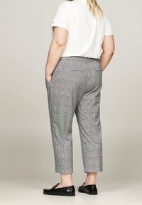 Šedé kárované zkrácené kalhoty s tailored střihem, které mají kapsy a zapínání na knoflík. Kombinované s bílým tričkem a černými botami.