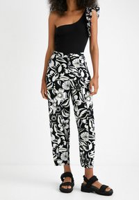 Haut noir à une épaule avec un détail de volants floraux, associé à un pantalon taille haute à motifs noir et blanc et des sandales noires épaisses.