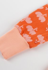 Oranger Stoff mit hellrosa, wolkenähnlichen Mustern, ausgestattet mit einem gerippten rosa Bündchen und Druckknopfdetails zum Schließen.