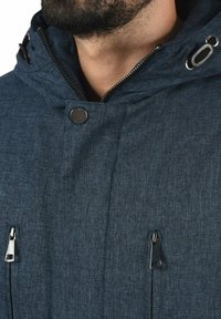 Marineblauw zip-up jack van een gestructureerde stof, verstelbare capuchon, metalen drukknoopsluiting en twee ritszakken aan de voorkant.