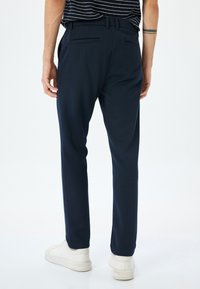 Navyblauwe, op maat gemaakte broeken met een gladde structuur, voorzien van achterzakken met paspel. Gestyled met een slim fit, gecombineerd met witte sneakers.