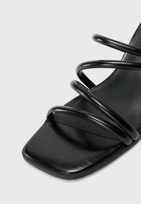 Black heeled sandal with a square toe. Features four metallic spiral straps and a smooth textured insole. Crafted from synthetic material.