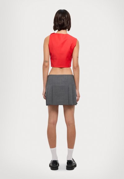 Červený top bez rukávů s kratším střihem v kombinaci s šedou skládací mini sukní. Tento outfit se vyznačuje jednoduchým designem s vodorovnými pruhy a černými botami.