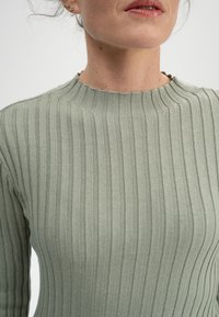 Helles grünes geripptes Stricktop mit hohem Kragen und strukturiertem Stoff. Verfügt über horizontale Linien und subtile Details am Kragen.