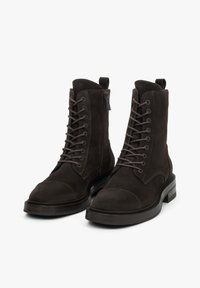 Ciemnobrązowe zamszowe buty wojskowe z okrągłym noskiem, sznurowane z przodu, z bocznym zamkiem błyskawicznym, z grubą czarną podeszwą i wzmocnionymi szwami.