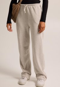 Light grey sweatpants with a relaxed fit, made of soft fabric, featuring a drawstring waist and side pockets. White sneakers complete the look.