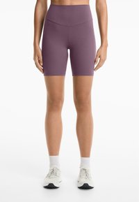Cykelshorts i solid mauve; hög midja. Slät textur, längd till mitten av låret och subtila sömdetaljer. Matchas med vita träningsskor.