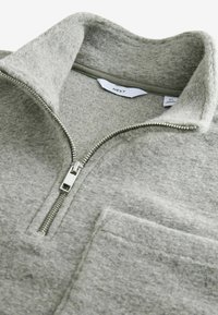 Grå fleecepullover med dragkedja i halsen, ribbad krage och framficka. Har mjuk textur och rena sömmar.