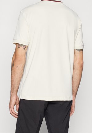 Homme portant un polo blanc uni à manches courtes et un pantalon noir, vu de dos avec des tatouages visibles sur les bras.