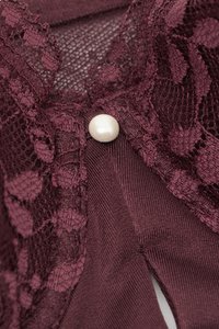 Vinrött spetsplagg med texturerad design, prytt med en framträdande knapp av pärlemor och fina blomster mönster längs kanten.