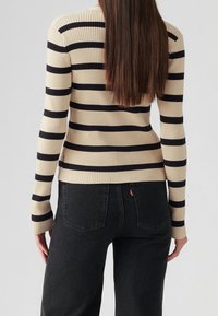 Beżowo-granatowy sweter w prążki, z dzianiny prążkowanej, z długimi rękawami i dopasowanym krojem. Do tego ciemne dżinsy z charakterystycznym przeszyciem.