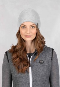 Szara dziana czapka z gładką fakturą i małą brązową metką. Połączona z ciemnoszarym kamizelką na zamek błyskawiczny z okrągłą łatką z logo.