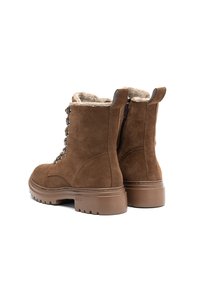 Bottes en daim marron à chevilles avec doublure en fourrure, œillets en métal, fermetures éclairs latérales, languettes de tirage et semelles en caoutchouc épaisses, présentées sous des angles arrière et latéral.