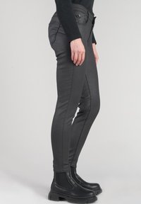 Pantaloni elasticizzati neri con una vestibilità slim, caratterizzati da una texture liscia, dettagli di cucitura e abbinati a stivaletti neri alla caviglia.