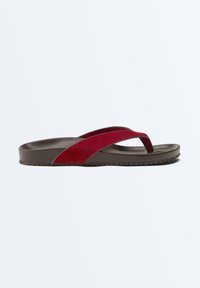Une sandale marron unique avec une semelle épaisse et une large bride en daim rouge traversant le pied et entre les orteils.