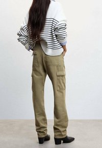 Maglione a righe bianche e nere sopra pantaloni cargo verde oliva con tasche, abbinato a stivali neri con tacco; lavorazione a maglia testurizzata e vestibilità comoda.