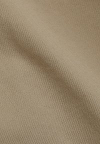 Gros plan d'un tissu beige avec une fine texture côtelée diagonale et des plis doux visibles sur toute la surface.