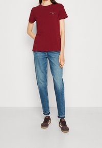 Camiseta de algodón burdeos con mangas cortas y cuello redondo, combinada con jeans de mezclilla azul claro y zapatillas de ante marrón.