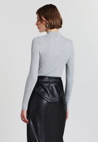 Grauer, gerippter Langarmoberteil mit hohem Kragen, kombiniert mit einem eleganten schwarzen Lederrock mit verborgenen Reißverschluss und glatter Textur.