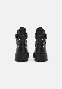 Černé kožené kotníkové boty s kovovými hřebíky, robustní podrážkou a páskovými detaily na zadní straně. Hladký povrch s matným finišem.