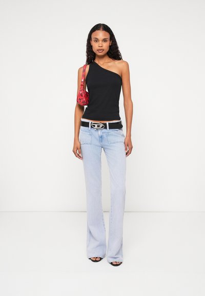 Haut noir à une épaule, jeans flare bleus clairs, et sac à main rouge à motifs. La ceinture possède une boucle argentée. Sandales à talons noires.