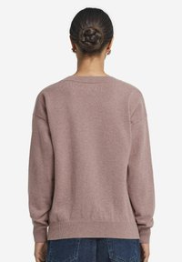 Ljusrosa stickad tröja med rund hals, sänkta axlar och ribbade ärmslut. Mjuk textur och avslappnad passform, matchad med mörkblå jeans.