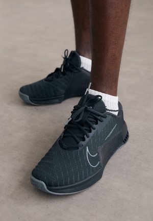 Sorte atletiske sko med en mesh-overdel, teksturerede sidepaneler og en gummisål. Har snørebånd og en diskret logoakcent.