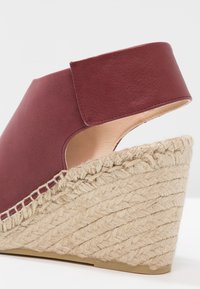 Sandale espadrille à talon compensé avec plateforme en jute tressée et tige en cuir bordeaux avec une large bride à la cheville.