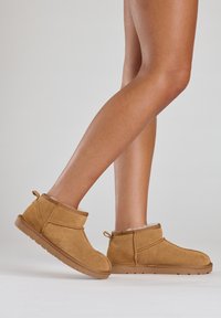 Bottines en cuir suédé beige avec une doublure intérieure douce, un bout arrondi et une languette de tirage. La semelle est plate avec une texture antidérapante pour une meilleure adhérence.