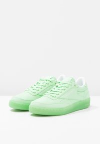 Gröna kanvasnikar med en slät textur, med ett vitt innerfoder och genomskinlig grön sula, som visar en klassisk låg toppdesign.