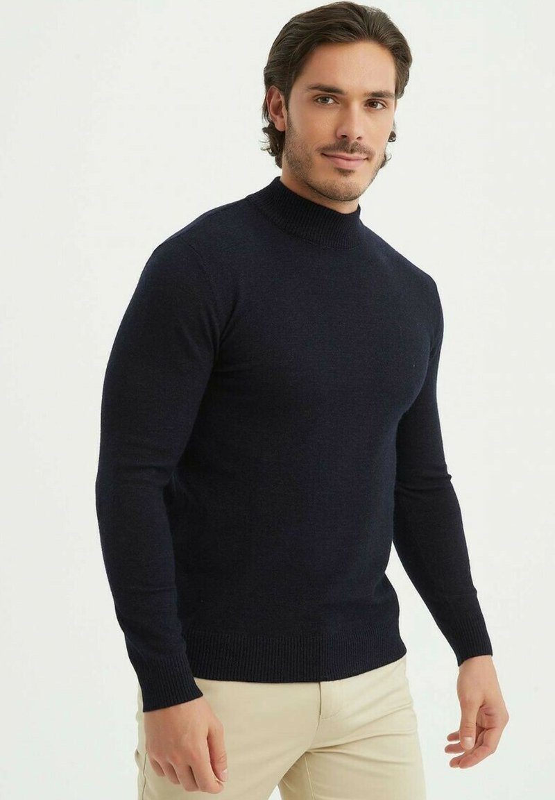 Pull en tricot bleu marine avec un col montant, des manches longues et des poignets et un bas côtelés. Le matériau semble doux avec une texture lisse.