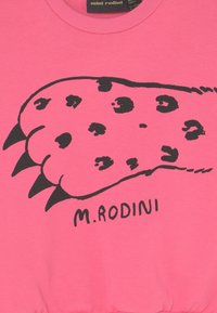 Rosa sweatshirt med en stor svart tassavtrycksdesign med fläckar och klor, samt texten "M. RODINI" under grafiken.