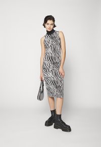 Abito midi con stampa zebra in bianco e nero, caratterizzato da un collo alto. Abbinato a stivali con plateau neri e una borsa a tracolla. 