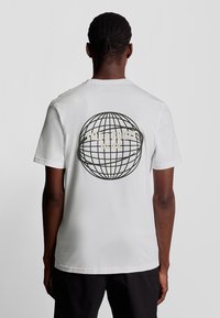 Hvid bomulds T-shirt med korte ærmer, der har et stort globus grafik og teksten "Alte&Scott EST 1874" på ryggen.