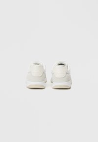 Bílé a šedé tenisky s hladkým koženým a semišovým povrchem, s texturovaným límcem na patě, plochými tkaničkami a gumovou podrážkou.