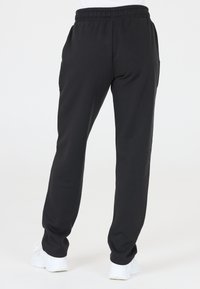 Svarta sweatpants med elastisk midja, sidofickor och avsmalnande ben, ihop med vita sportskor. Slät tygtextur.