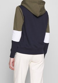Sudadera con capucha en navy, verde oliva y blanco. Presenta bloques de color contrastantes y puños acanalados. Tejido suave con un ajuste relajado.