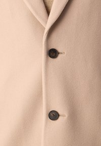 Abrigo de mezcla de lana beige con cuello de muesca, dos botones negros y una textura suave. El diseño incluye un acento de costura detallada.