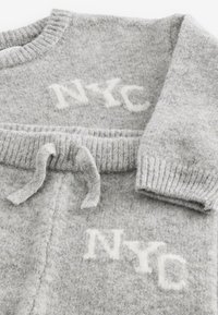 Maglione grigio lavorato a maglia con polsini e orlo a coste, con la scritta bianca "NYC" ricamata sul davanti e un dettaglio a coulisse in vita.