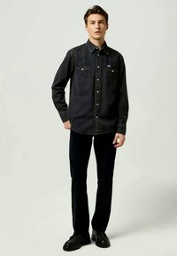 Camisa de mezclilla negra con cierre de botones a presión, dos bolsillos en el pecho y costuras en contraste. Combina con pantalones oscuros y zapatos negros. Textura suave.