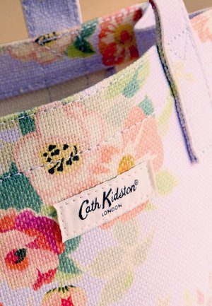 Virágmintás szövet bevásárlótáska varrott fogantyúkkal és egy fehér címkével az elején, amelyen a "Cath Kidston London" felirat olvasható.