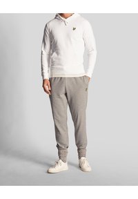 Felpa bianca con cappuccio, munita di lacci e tasca a marsupio, abbinata a pantaloni jogger grigi affusolati con logo ricamato. Sneakers bianche.