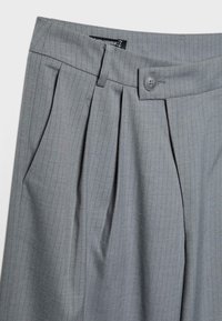 Pantalon gris à fines rayures, avec plis devant, poches latérales, passants pour ceinture et fermeture de taille boutonnée.