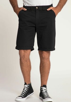 Shorts en coton noir avec des ourlets roulés, poches frontales et fermeture à un bouton. Portés avec des baskets montantes noires.