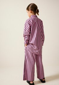 Oversized Hemd mit rosa und lila Streifen und weiten Hosen, aus glattem Stoff gefertigt. Verfügt über lange Ärmel und Seitentaschen. Einfaches Design.